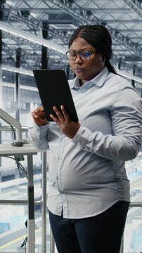 Vertical video Portrait of smiling woman reviewing semiconductors smart factory schematics. Cheerful african american businesswoman oversees infrastructure layouts using EDA software in industry 4.0
