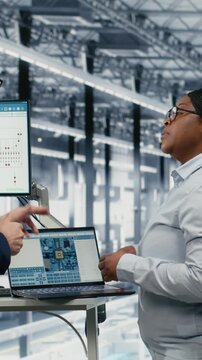 Vertical video Businesspeople team optimizes PCB smart factory workflow using EDA software on laptop. Employees using notebook simulation program tracking semiconductor production circuit layout