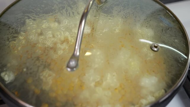 Cooking popcorn popping inside a pot with glass lid. Close-up view of corn kernels popping in a hot pan on a stovetop with a transparent glass lid, making a delicious and fun snack