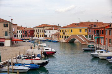 Obraz premium Main canal of Murano with colorful houses moored boats and brick arch bridge