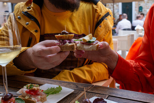 Two friends sharing Venetian cicchetti at outdoor table with white wine and aperitivo