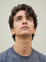 Naklejka premium A thoughtful young adult male with curly hair gazing up at something beyond the frame of the photo.