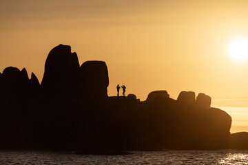 Obraz premium Rock formations silhouette with couple standing during sunset creating scenic coastal dramatic landscape view