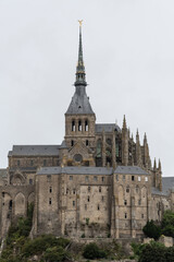 Obraz premium Mont Saint Michel abbey rising above landscape with historic architecture and cloudy sky background