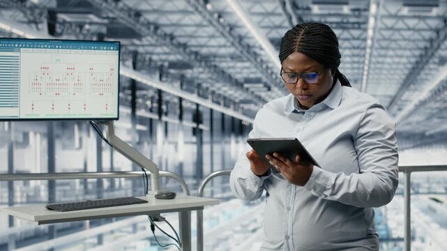 Portrait of smiling woman reviewing semiconductors smart factory schematics. Cheerful african american businesswoman oversees infrastructure layouts using EDA software in industry 4.0 plant, camera B