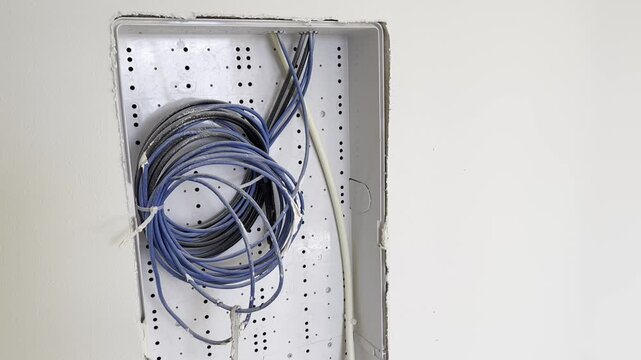 Open electrical box with bundled wires inside a wall during construction or renovation, close up.