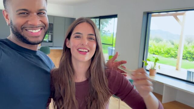 A happy young couple celebrates buying their dream home, proudly holding up the keys. Their excitement for this new chapter is palpable in their modern, bright living space.