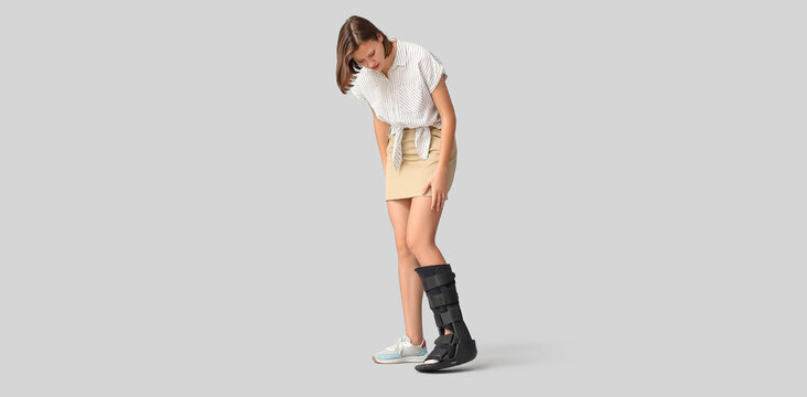 Young woman with broken leg on light background