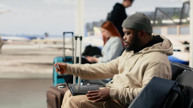 Black man digital nomad working on laptop in busy airport terminal lounge, modern remote professional illustrates location independent work and global mobility. Ability to work anywhere.