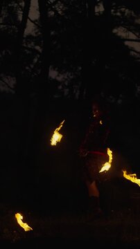 Lone performer in a dark forest night manipulating swirling flames, creating glowing arcs of fire and sparks that illuminate the surrounding shadows and trees