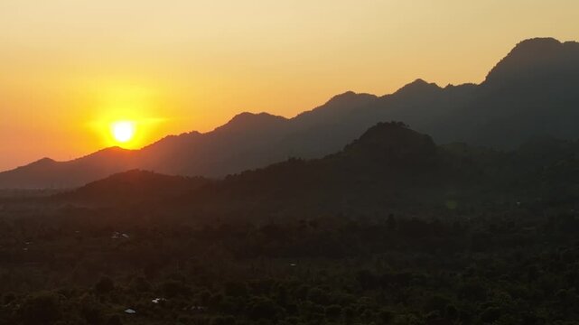 Aerial view of the golden sunset over silhouetted mountain peaks and a lush green valley in Kawah Ijen, East Java, Indonesia.