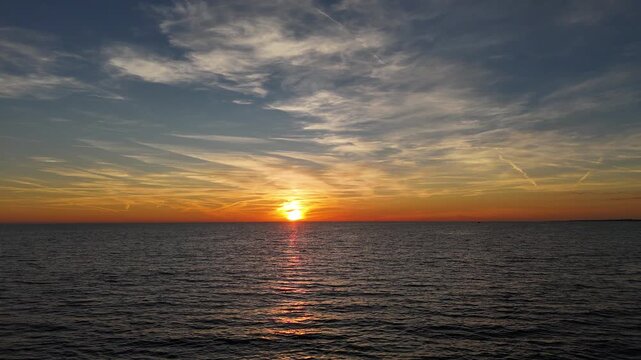 Sunset paints the sky with vibrant colors over calm waters at the beach during a peaceful evening