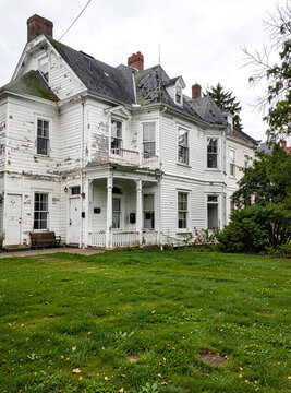 An old and abandoned white house with peeling paint on a cloudy day.