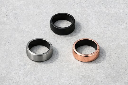 Trio of modern smart rings in black, silver, and rose gold on concrete surface. concept of fashion technology, accessory design, minimalist style, innovation, contemporary jewelry