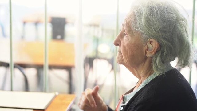 A grandmother sitting in a restaurant chair, wearing headphones and talking to someone else