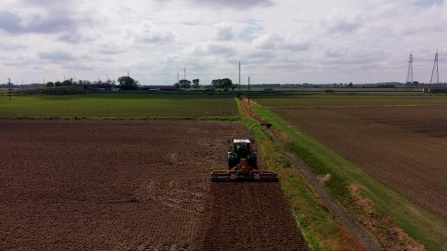 Tractor Plowing Field: A modern tractor cultivates a vast expanse of fertile farmland, preparing the soil under a cloudy sky, signifying the ongoing work in agriculture.