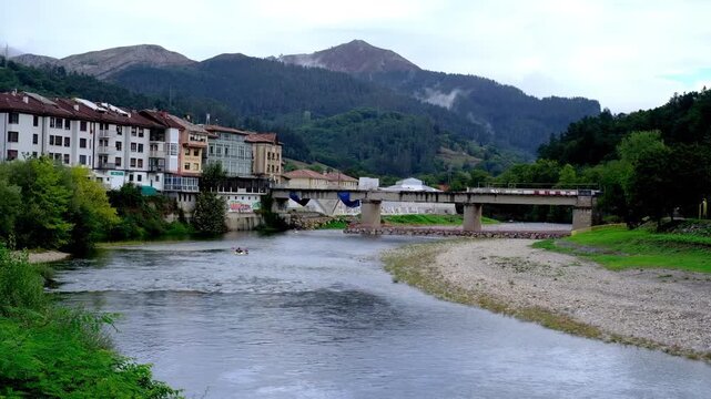Scenic view of Arriondas town in Asturias, Spain, featuring the Sella River flowing under a bridge with green mountains in the background