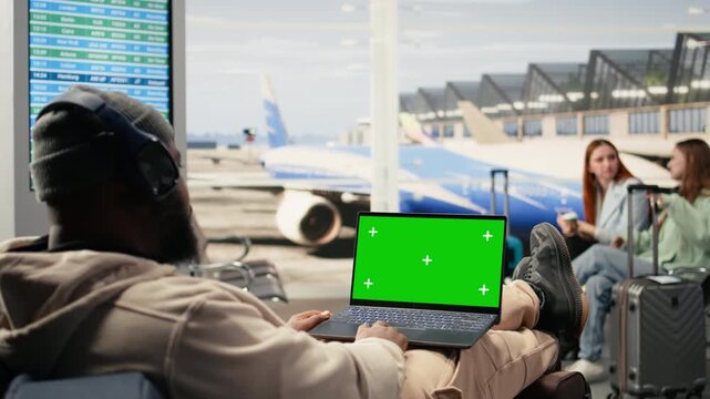 Green screen laptop with African American travelers in crowded airport waiting area before flight departure. Luggage and boarding procedures in the background, nomadic lifestyle.