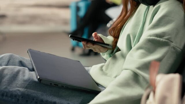Gen z remote worker using phone in a crowded airport terminal lounge, air travel and nomadic lifestyle concept. Location independent girl with flexible career, online business mobility.