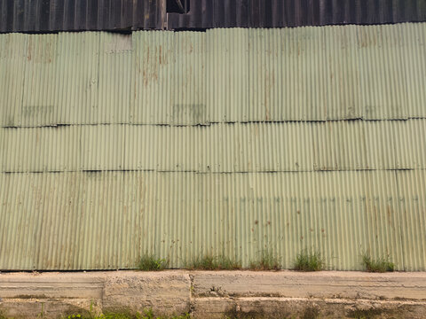 Distressed pale green corrugated metal wall with rust spots. Industrial texture of a weathered warehouse exterior featuring oxidized steel sheets and vertical patterns