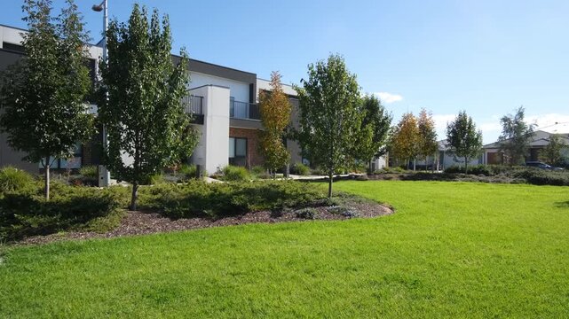 A landscaped communal garden, green lawn in front of a row of modern double-storey townhouses in a newly developed suburban estate in Tarneit, Melbourne, Australia.&nbsp;Well-maintained street environment