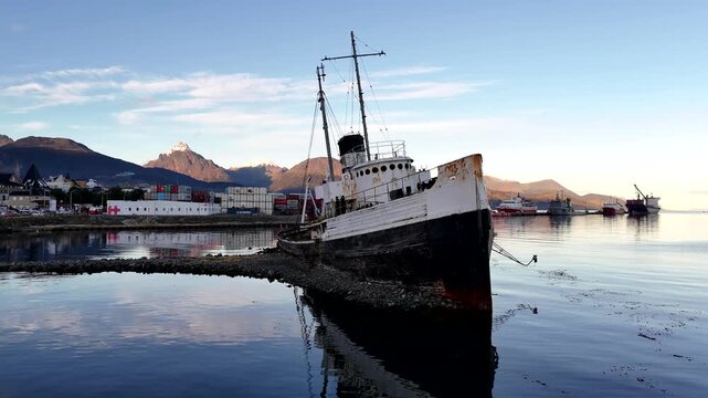 Static aerial shot of the grounded Saint Christopher shipwreck in Ushuaia harbor, with the Martial Mountains and Beagle Channel in the background
