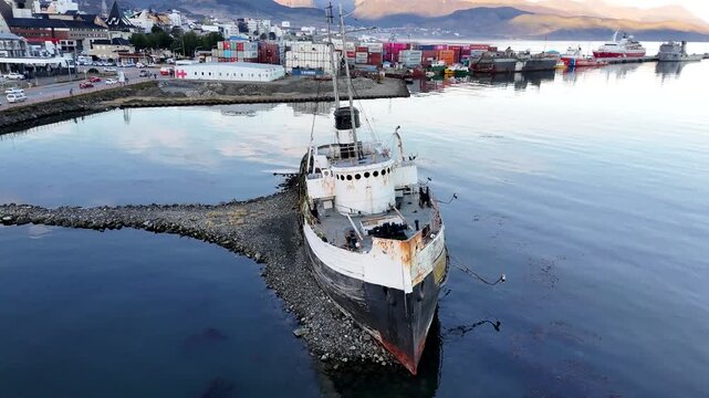 Cinematic drone orbit moving clockwise around the Saint Christopher shipwreck, revealing the industrial harbor, shipping containers, and Beagle Channel