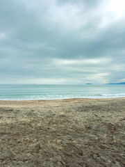 Fototapeta premium Cloudy sky over a beach with gentle waves and distant ships on the horizon during an overcast day in a coastal area