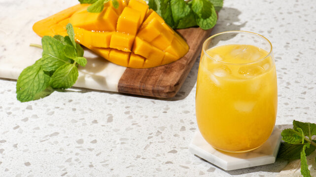 Summer mango drink mocktail with ice and mint on terrazzo countertop, bright refreshment with copy space