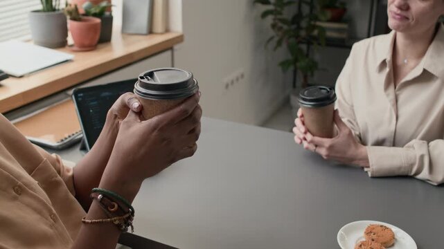 High angle close up shot of two unrecognizable women drinking coffee from plastic cups while taking break from office work