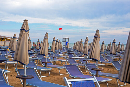 Beach chairs and umbrellas lined up under cloudy sky near ocean with red flag raised in late afternoon