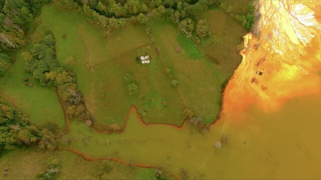 Aerial view of the toxic orange tailings pond flooding the green fields and surrounding forest of the sunken village Geamana, Alba County, Romania.