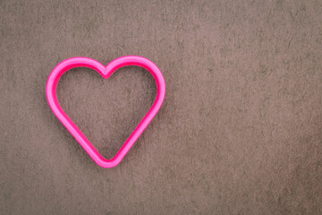 Fototapeta premium Bright pink heart shape rests on a gray surface near the edge during daytime
