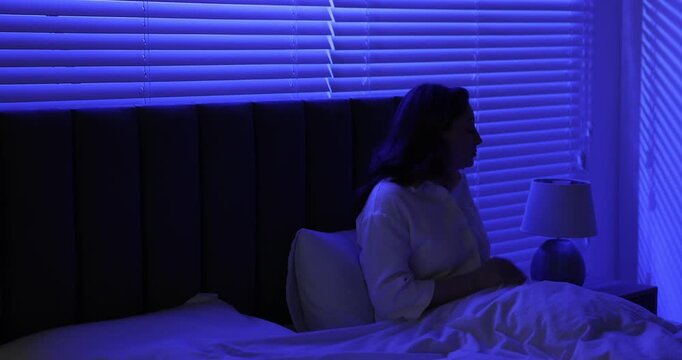 Woman putting book onto nightstand, turning off night lamp and lying down for sleep in bed at home