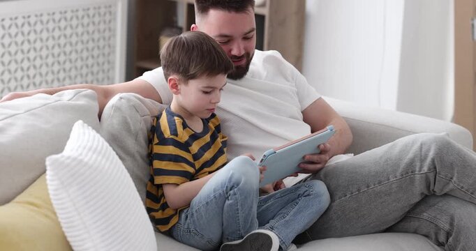 Father and his son using tablet on sofa at home