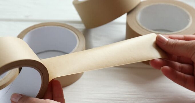 Eco-friendly packaging. Woman with rolls of masking tape at white wooden table, closeup