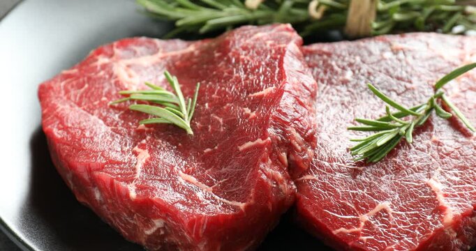 Raw beef steaks and rosemary on grey table, closeup. Camera moving right