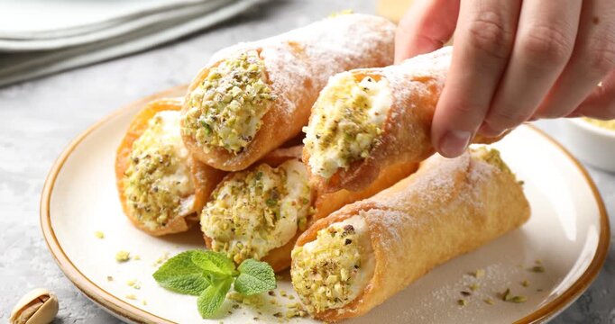 Woman taking delicious cannoli with cheese and pistachios at grey table, closeup