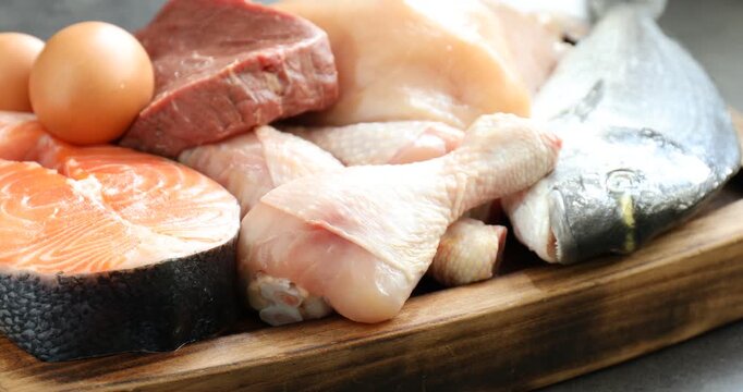 Different types of fresh raw meat, fish and eggs on table, closeup. Camera moving right