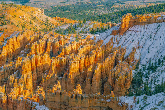 Intricate orange hoodoo formations in Bryce Canyon National Park partially covered in snow during a crisp, sunlit winter day.