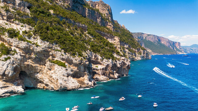 Aerial view of motorboats and yachts navigating along the monumental limestone cliffs of Cala Mariolu, Gulf of Orosei, Sardinia, Italy