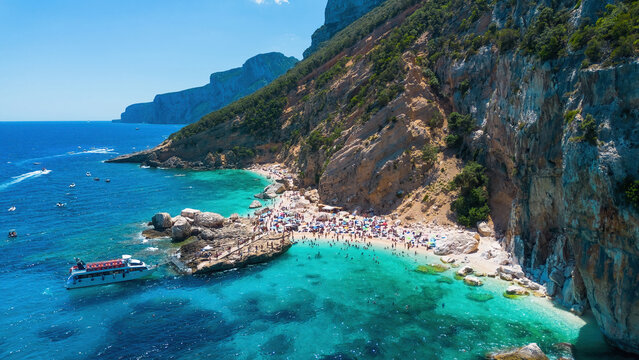 Aerial view of tourists landing from an excursion boat at Cala Mariolu beach, Gulf of Orosei, Baunei, Sardinia, Italy