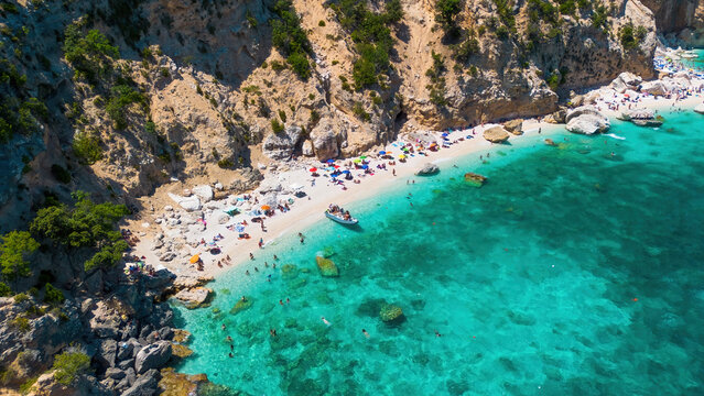 Aerial view of Cala Mariolu beach with people sunbathing and swimming in turquoise crystal clear water, Gulf of Orosei, Baunei, Sardinia, Italy