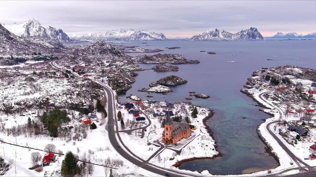 Aerial view of Kabelvag Church surrounded by a snowy coastal landscape and winding roads in Nordland, Norway.