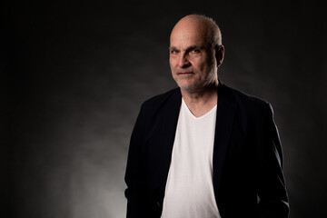 Fototapeta premium Bald middle aged man in a dark suit jacket and white t shirt posing with a serious expression