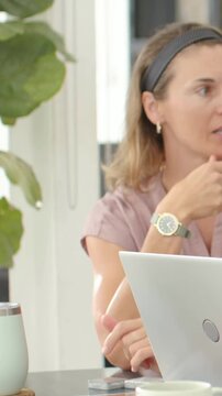 Vertical video: Starting call, gesturing woman in pink blouse touching chin at home with laptop mug