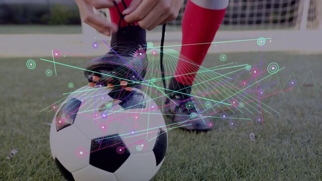 Teen soccer player placing foot on ball, tying cleat laces for practice while HUD overlay tracking