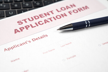 Fototapeta premium A student loan application form rests on a laptop keyboard with a blue ballpoint pen, emphasizing the financial side of higher education and college planning.