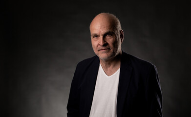 Fototapeta premium Volker Schlondorff, an aging bald man, is posing for a portrait in a studio