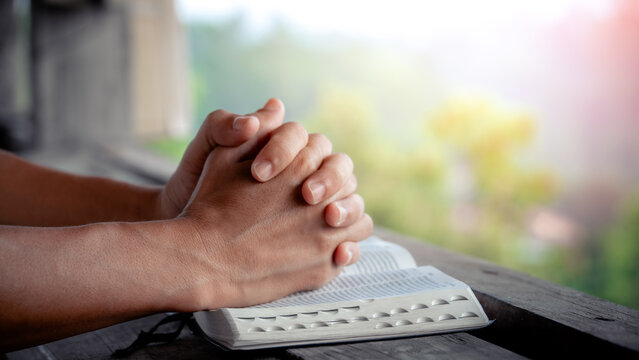 Close up of a man praying, hands clasped together on Bible, devotional concept.